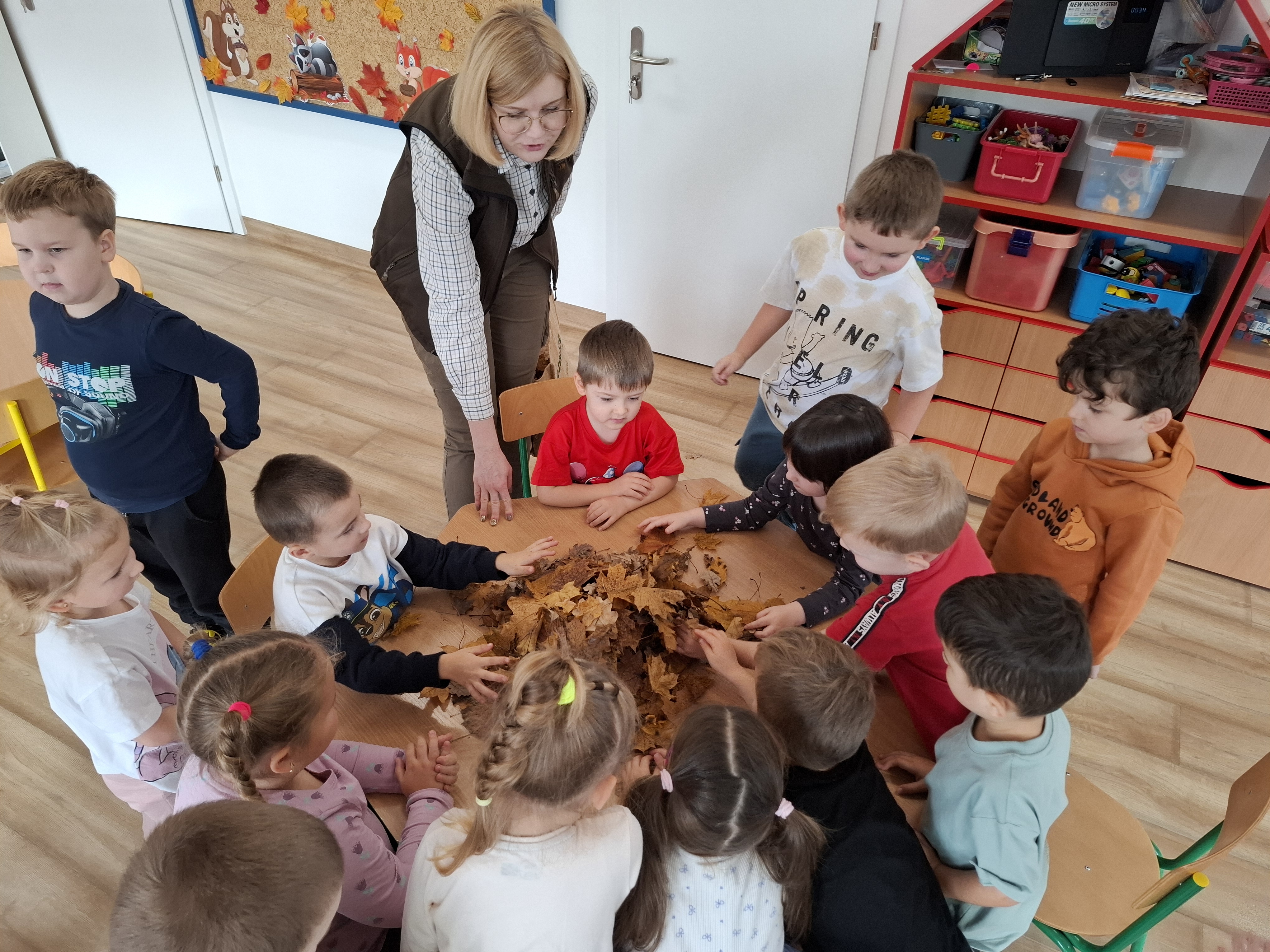 Dzieci przysypują jeża liśćmi