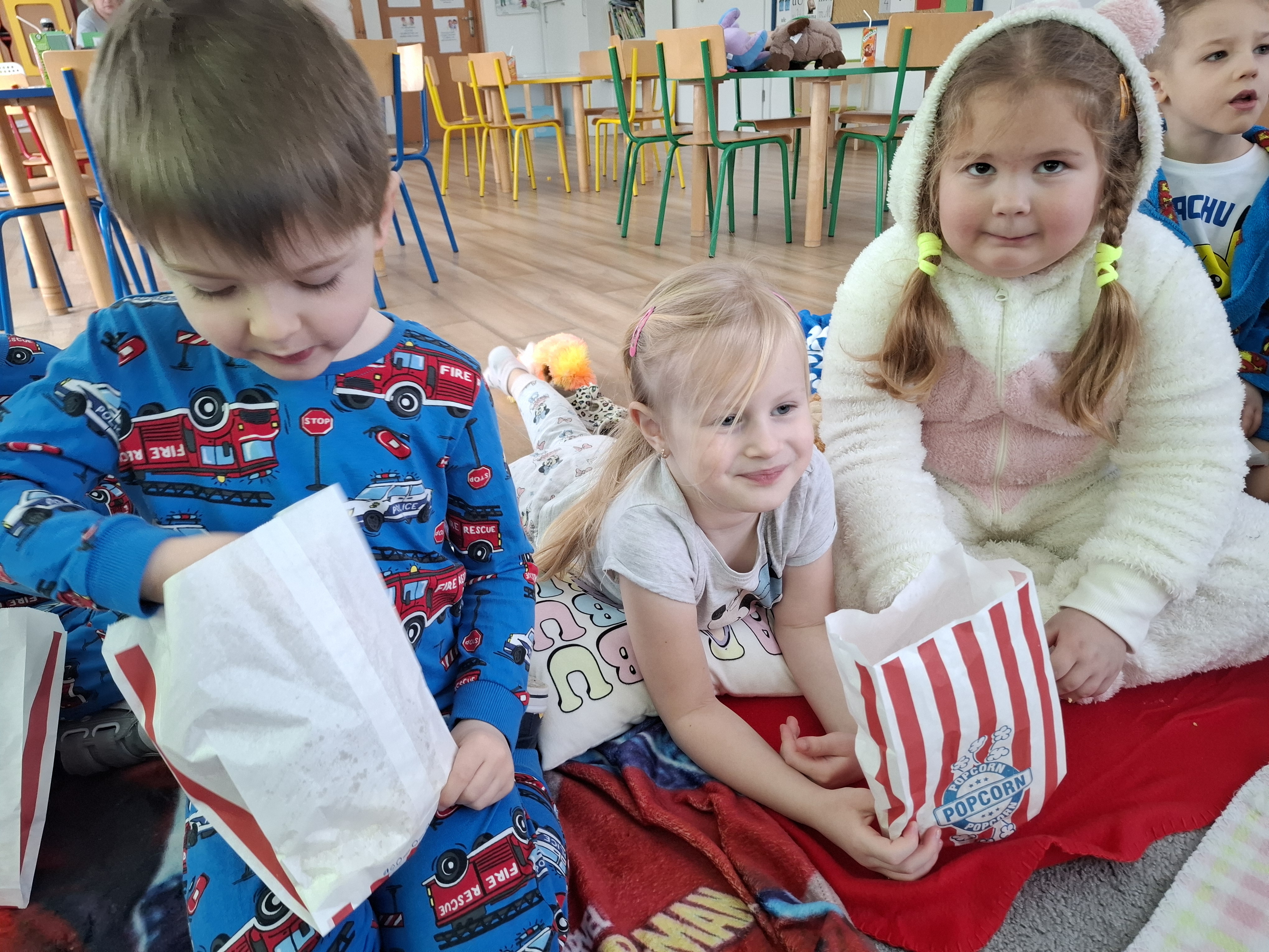 Dzieci jedzą popcorn oglądając bajkę